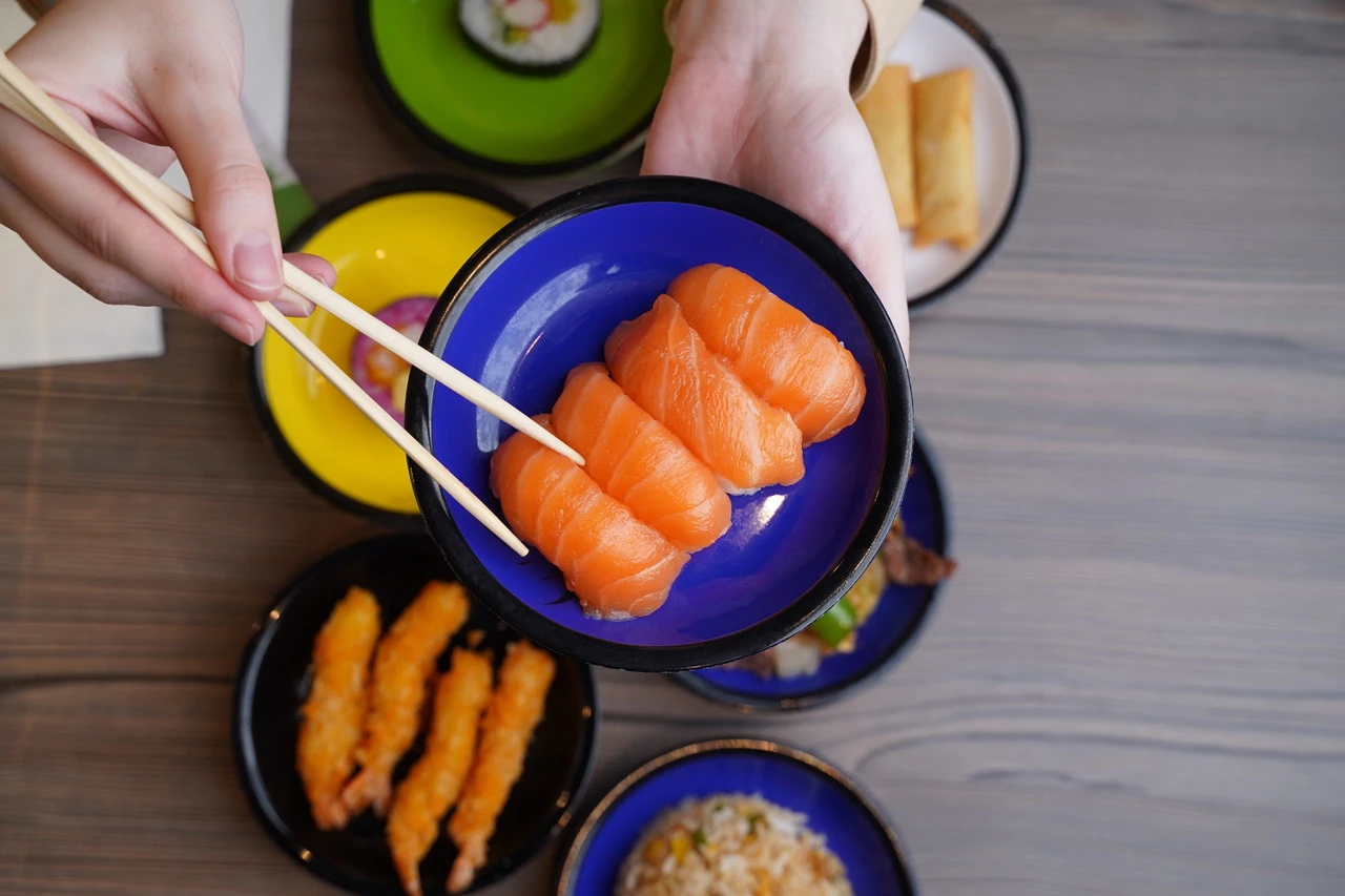 Colorful sushi assortment with salmon nigiri, spring rolls, and fried shrimp. Chopsticks pick up salmon sushi.